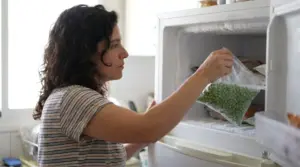 אישה מוציאה שקית אפונה ללא מותג מהמקפיא הביתי