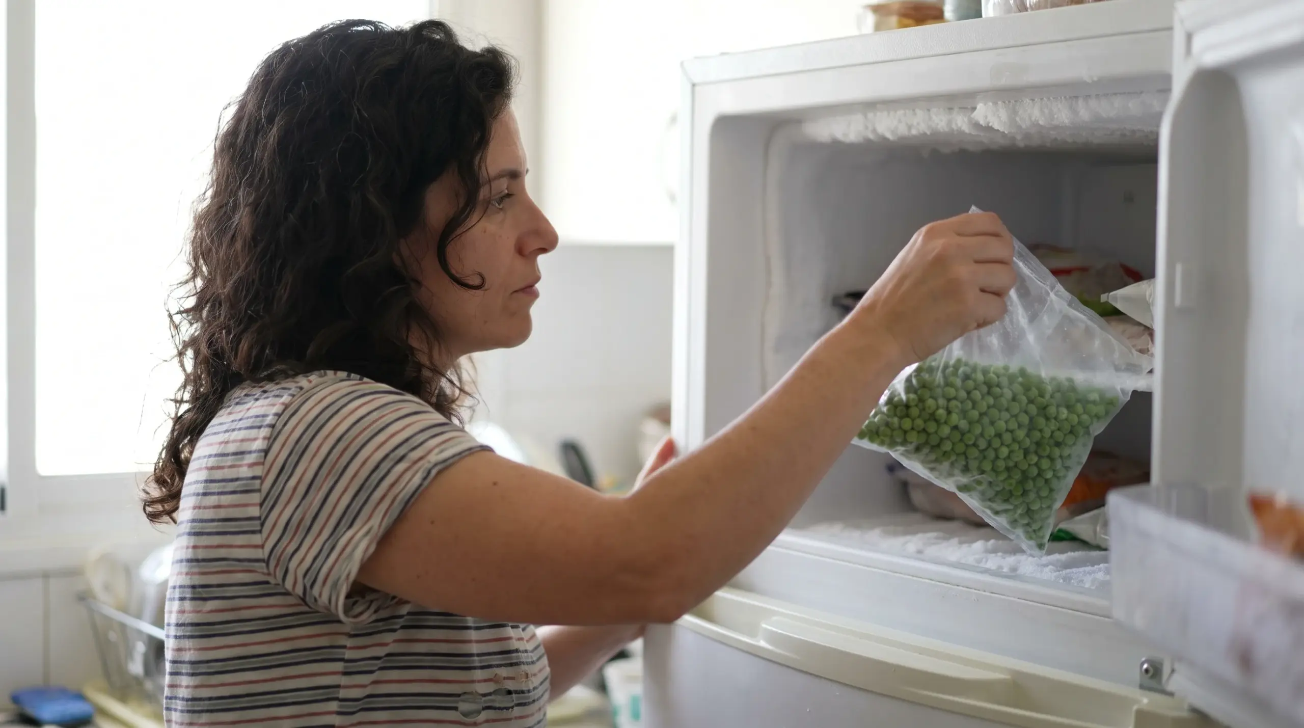 אישה מוציאה שקית אפונה ללא מותג מהמקפיא הביתי